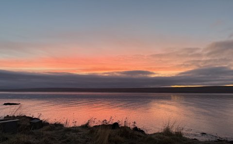 Blessuð nýárssólin séð af sjávarbakkanum við Bakkatún á nýársdag.